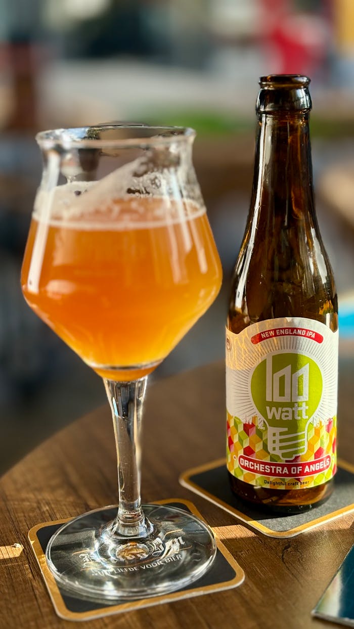 Close-up of a craft beer glass and a 100 Watt beer bottle on a table.