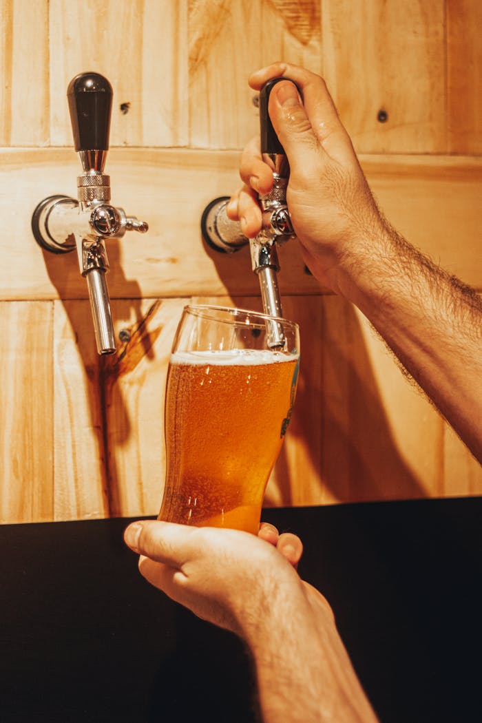 Offerings A person pouring refreshing craft beer into a glass from a tap against a wooden wall.